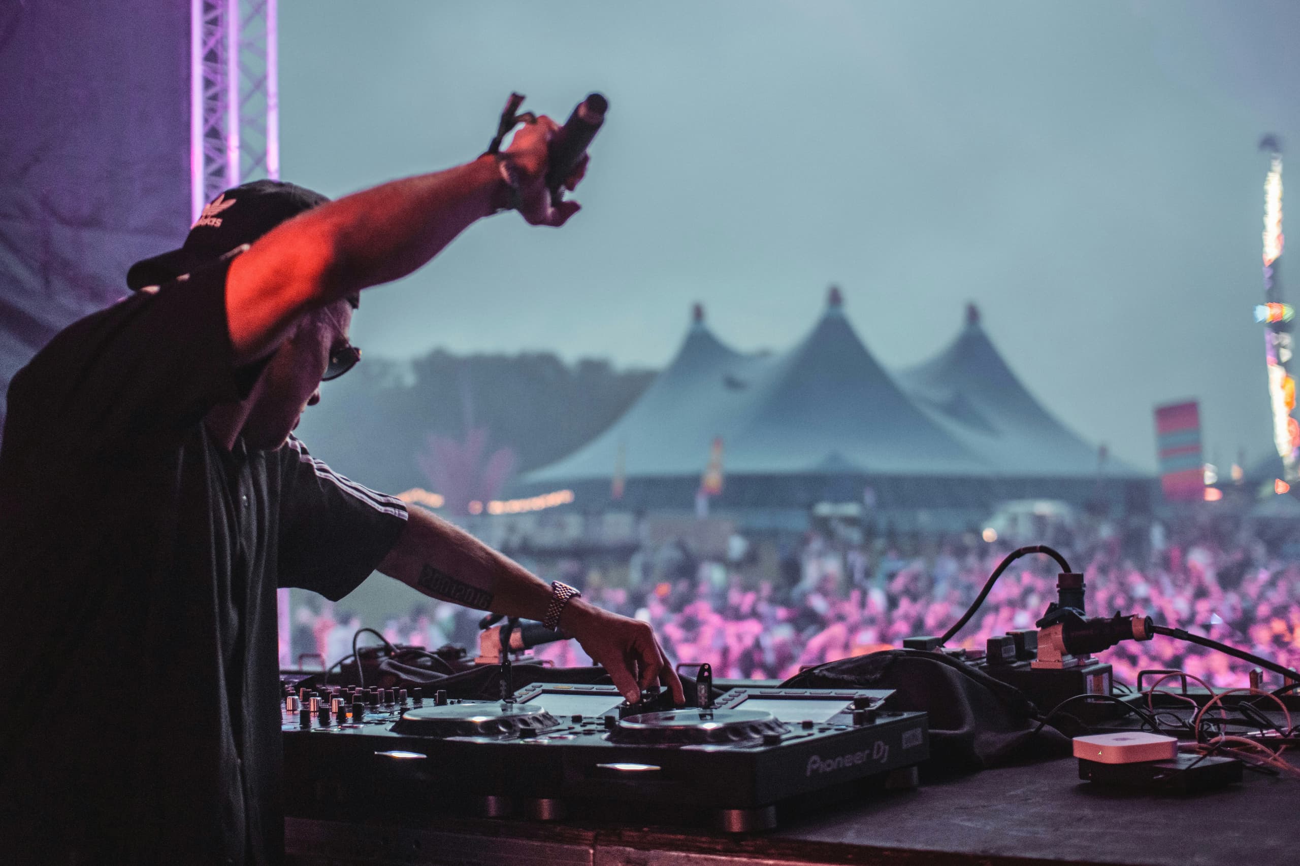 Laser lights and pyrotechnics over a packed festival crowd at dusk